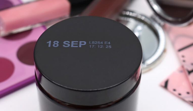 Black cosmetic jar with white thermal inkjet print surrounded by makeup products